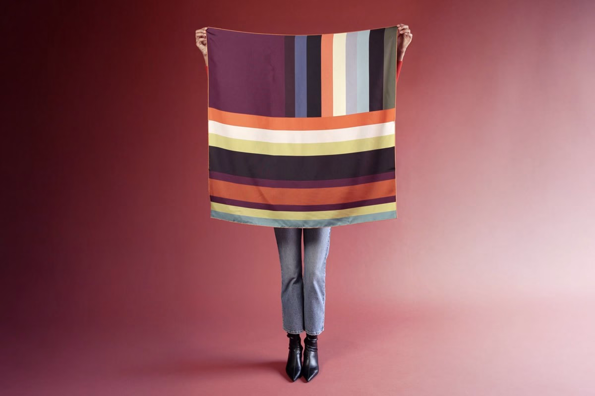 Una ragazza in jeans che mostra un grande foulard in seta Barbieri a fantasia.